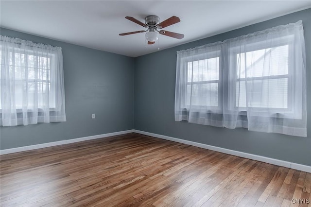 empty room with ceiling fan, a healthy amount of sunlight, wood finished floors, and baseboards