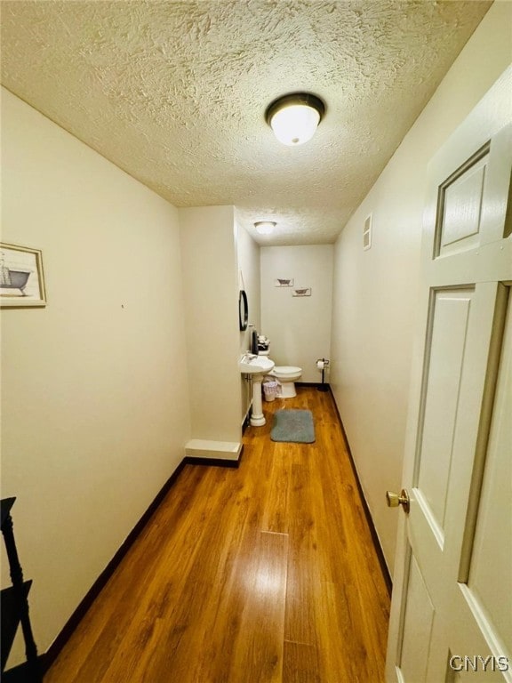 hall featuring baseboards, wood finished floors, and a textured ceiling