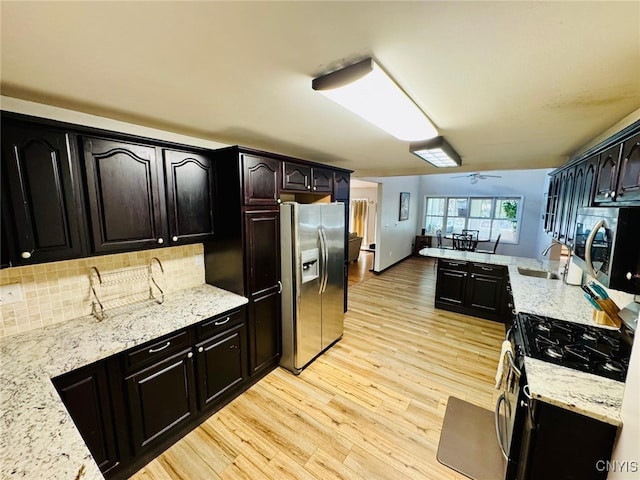 kitchen featuring a sink, appliances with stainless steel finishes, light wood-style floors, light stone countertops, and decorative backsplash