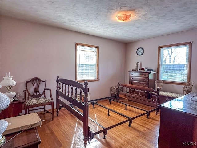 bedroom with light wood-style flooring, multiple windows, baseboards, and a textured ceiling