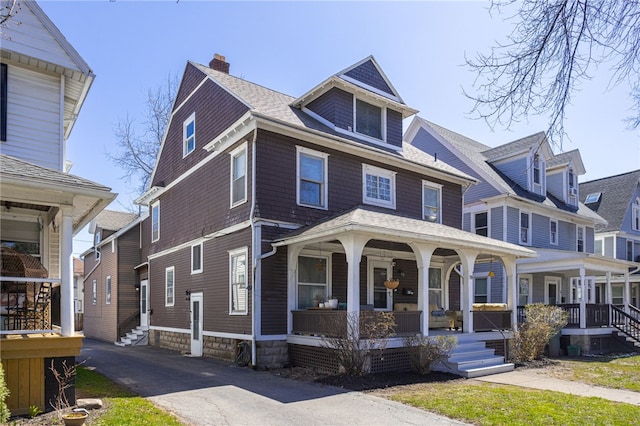 traditional style home with a porch, roof with shingles, and a chimney