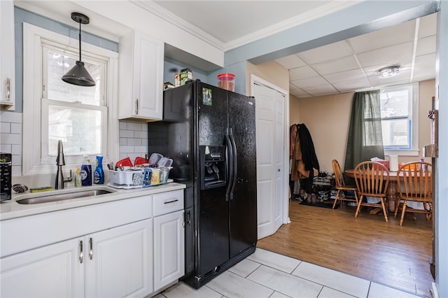 kitchen featuring tasteful backsplash, light tile patterned floors, white cabinetry, black fridge, and a sink