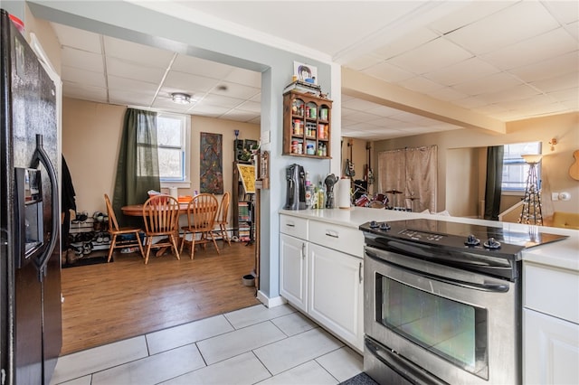 kitchen featuring stainless steel electric stove, a drop ceiling, white cabinets, black refrigerator with ice dispenser, and light tile patterned flooring