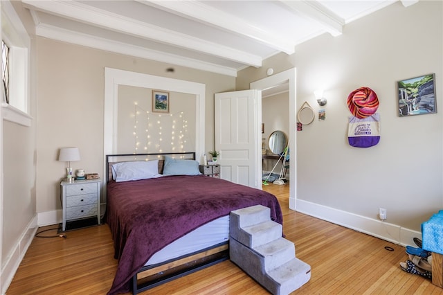 bedroom featuring light wood finished floors, baseboards, and beam ceiling