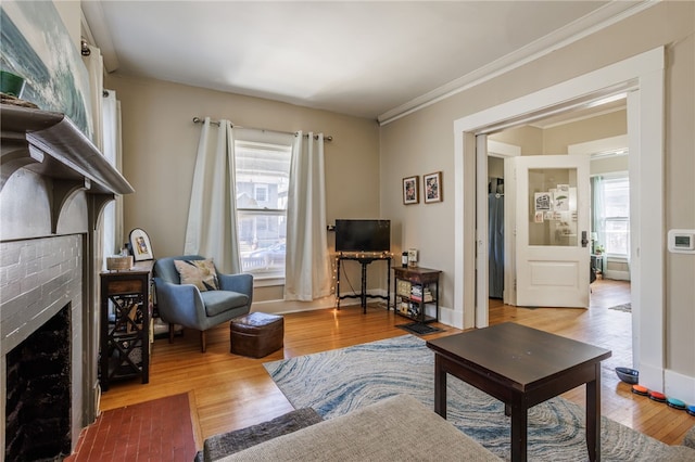 living room with a brick fireplace, ornamental molding, and wood finished floors
