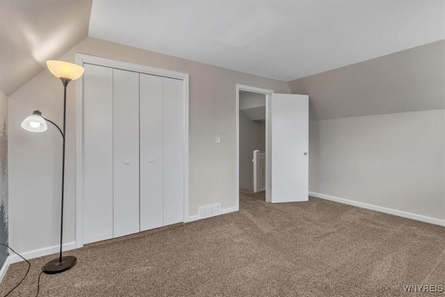 unfurnished bedroom with visible vents, baseboards, a closet, vaulted ceiling, and carpet flooring