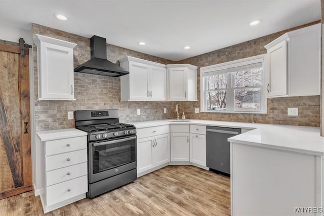 kitchen featuring light countertops, appliances with stainless steel finishes, wall chimney exhaust hood, and white cabinetry