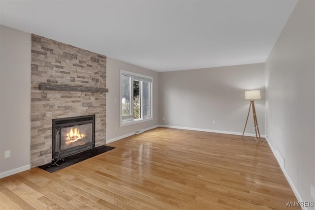 unfurnished living room with light wood-style flooring, visible vents, baseboards, and a stone fireplace