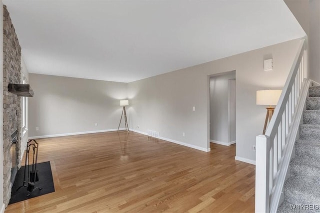unfurnished living room with visible vents, baseboards, light wood-style floors, a fireplace, and stairway