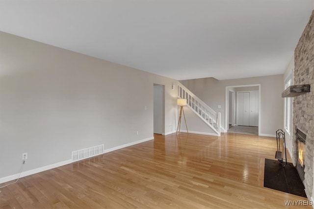 unfurnished living room featuring light wood finished floors, a stone fireplace, visible vents, and stairs