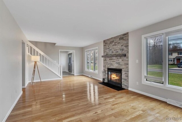 unfurnished living room featuring visible vents, baseboards, a stone fireplace, wood finished floors, and stairs