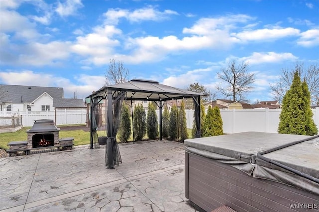 view of patio featuring a lit fireplace, a gazebo, a fenced backyard, and a hot tub