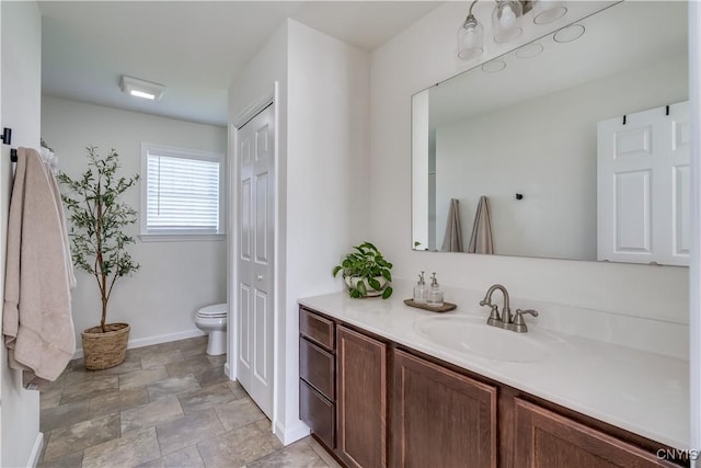 bathroom with toilet, stone finish floor, vanity, and baseboards