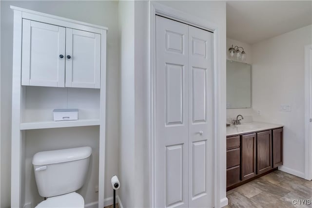 bathroom featuring toilet, a closet, vanity, and baseboards