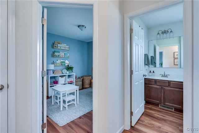hallway featuring visible vents, baseboards, a sink, and wood finished floors