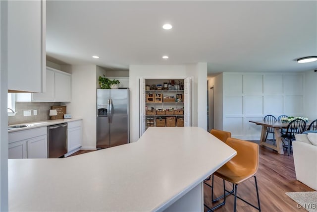 kitchen featuring a sink, light countertops, appliances with stainless steel finishes, a kitchen breakfast bar, and white cabinetry