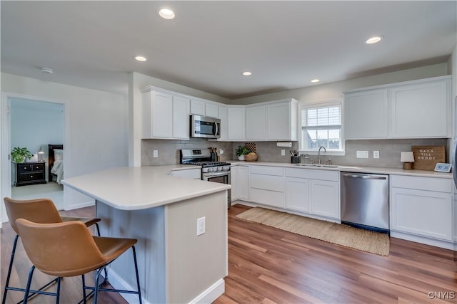 kitchen featuring a sink, appliances with stainless steel finishes, a peninsula, white cabinetry, and backsplash