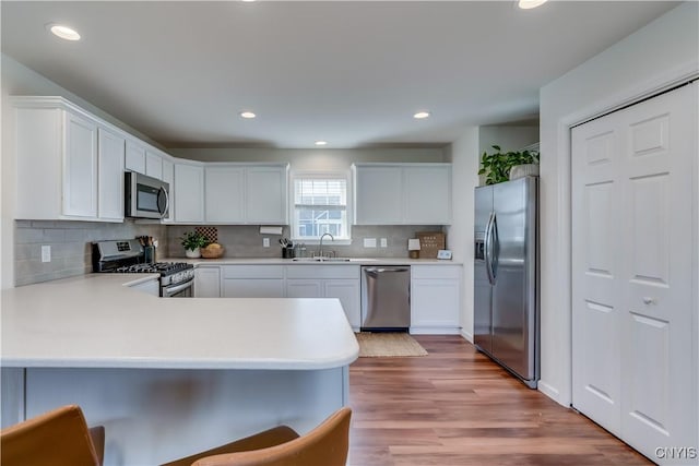 kitchen with a peninsula, light countertops, backsplash, stainless steel appliances, and a sink