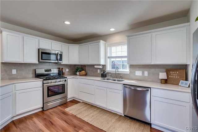 kitchen with white cabinets, a sink, light countertops, light wood-type flooring, and appliances with stainless steel finishes
