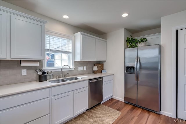 kitchen featuring a sink, light countertops, appliances with stainless steel finishes, light wood-style floors, and decorative backsplash