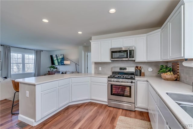 kitchen featuring open floor plan, a peninsula, white cabinetry, light countertops, and appliances with stainless steel finishes