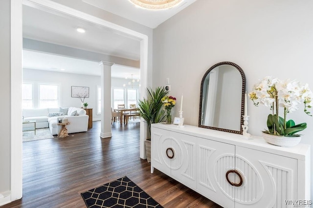 hallway featuring dark wood finished floors, ornate columns, and a chandelier