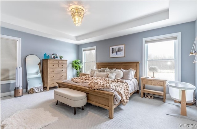 bedroom with carpet floors, a tray ceiling, and baseboards