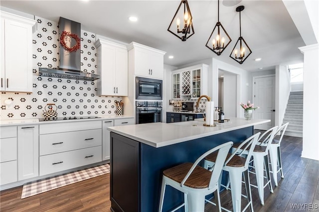 kitchen featuring black appliances, wall chimney range hood, dark wood-type flooring, a kitchen breakfast bar, and recessed lighting