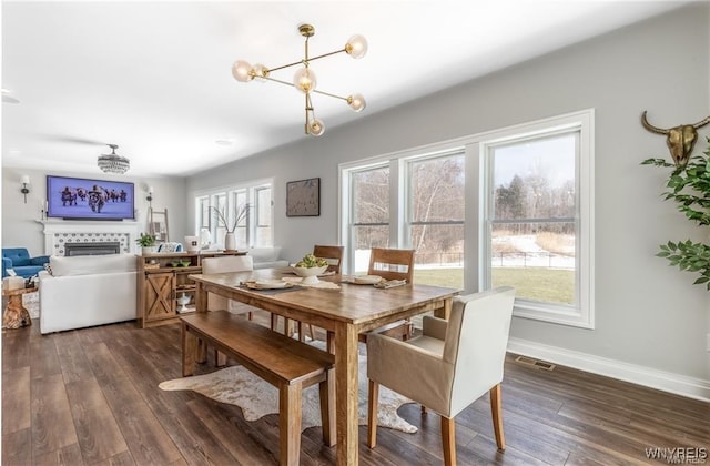 dining area featuring dark wood-type flooring, a chandelier, a fireplace, and baseboards