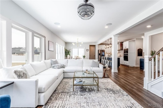 living room featuring a chandelier, dark wood-style flooring, stairs, recessed lighting, and decorative columns