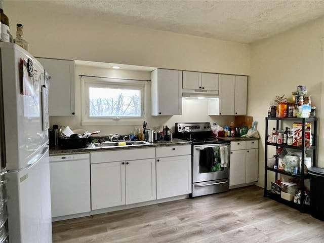 kitchen with a textured ceiling, under cabinet range hood, dark countertops, and white appliances