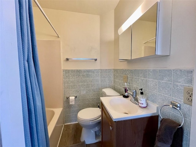 bathroom featuring tile walls, toilet, shower / bathtub combination with curtain, vanity, and a wainscoted wall