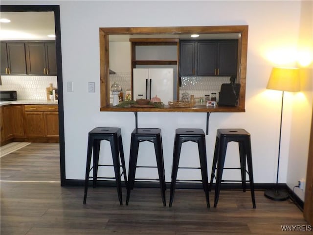 kitchen with dark wood-style flooring, backsplash, a kitchen breakfast bar, and white fridge with ice dispenser