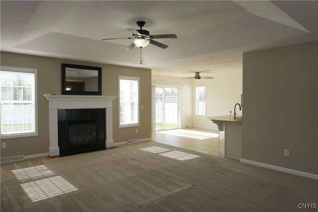 4828 Lighthouse Village Cir, Clay, NY 13088 - unfurnished living room featuring visible vents, a sink, a ceiling fan, a fireplace, and a tray ceiling