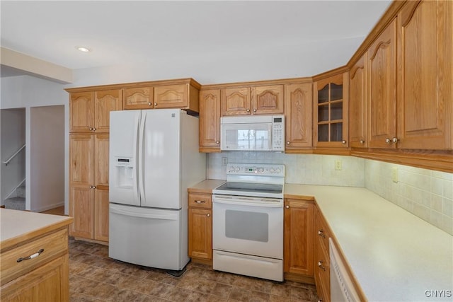 kitchen with glass insert cabinets, light countertops, white appliances, and tasteful backsplash
