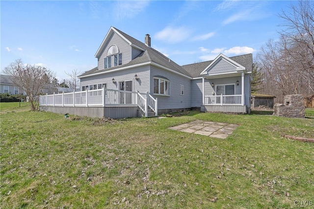 rear view of house featuring a lawn, a chimney, a wooden deck, and a patio