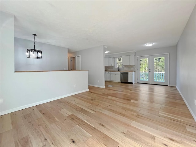 unfurnished living room featuring light wood-style floors, a sink, french doors, baseboards, and a notable chandelier