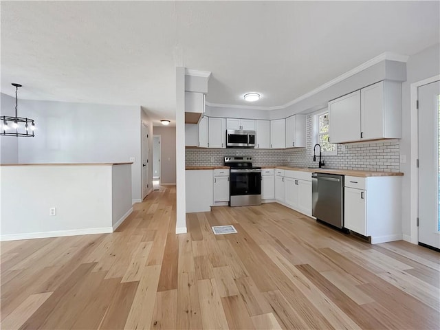 kitchen featuring baseboards, white cabinets, decorative backsplash, light wood finished floors, and appliances with stainless steel finishes