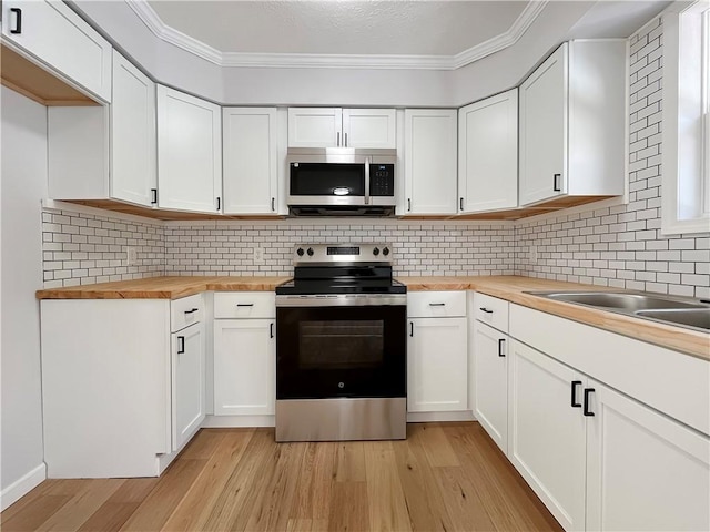 kitchen with light wood-style floors, butcher block counters, ornamental molding, stainless steel appliances, and decorative backsplash