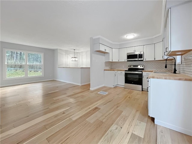 kitchen featuring visible vents, a sink, appliances with stainless steel finishes, light wood finished floors, and decorative backsplash