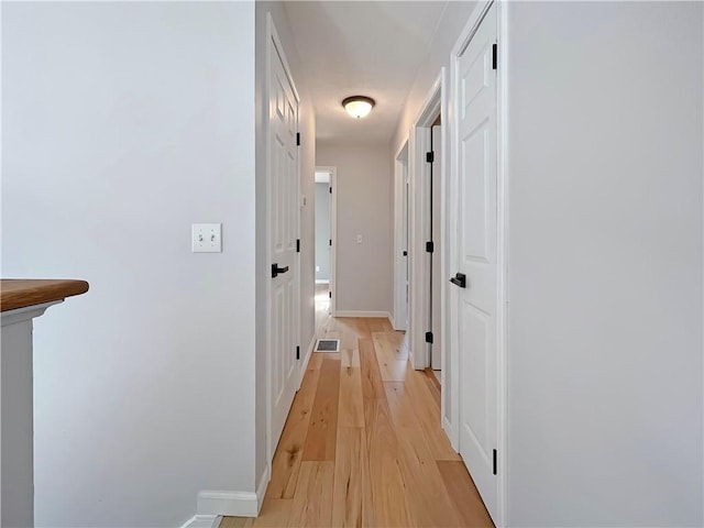 corridor with light wood finished floors, baseboards, and visible vents