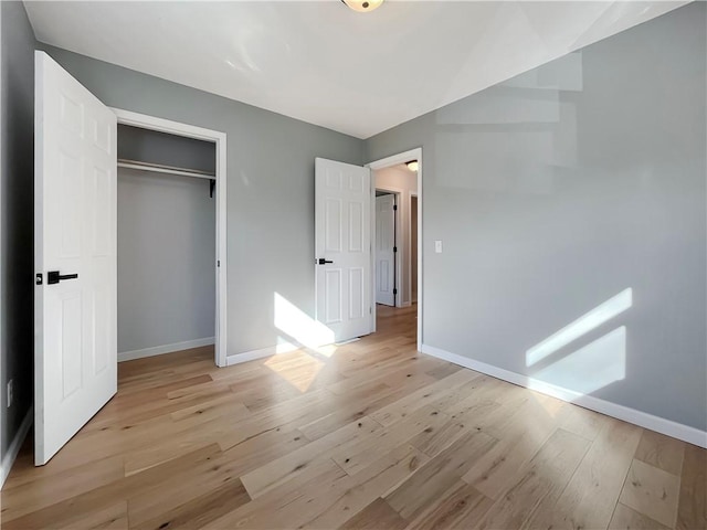 unfurnished bedroom featuring light wood-style flooring, a closet, and baseboards