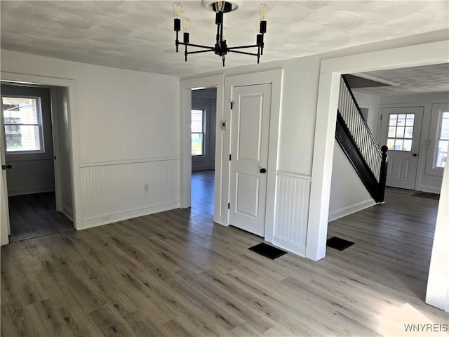 unfurnished dining area with stairs, a notable chandelier, plenty of natural light, and wood finished floors