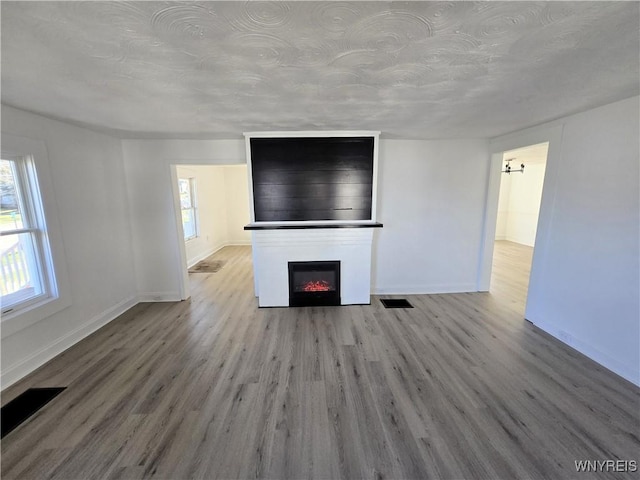 unfurnished living room featuring visible vents, a large fireplace, baseboards, and wood finished floors
