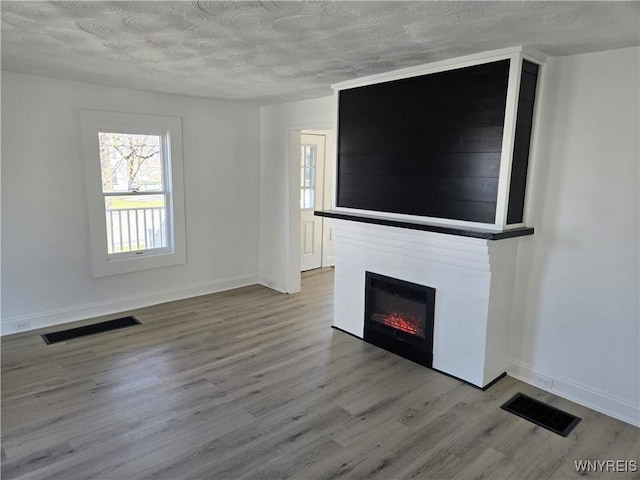 unfurnished living room featuring a glass covered fireplace, visible vents, a textured ceiling, and wood finished floors