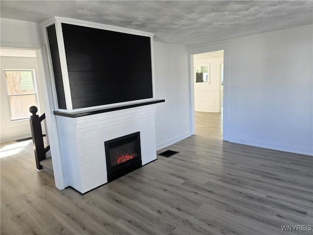 unfurnished living room with visible vents, a glass covered fireplace, and wood finished floors