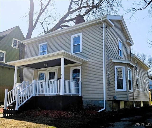 american foursquare style home featuring a porch and a chimney