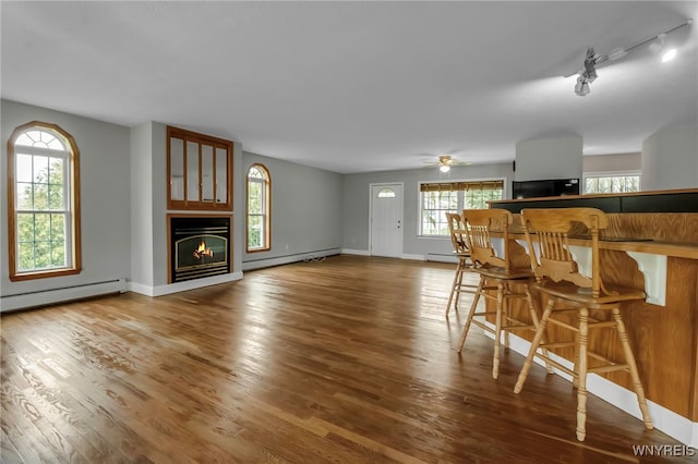living room featuring track lighting, wood finished floors, a baseboard heating unit, and a glass covered fireplace