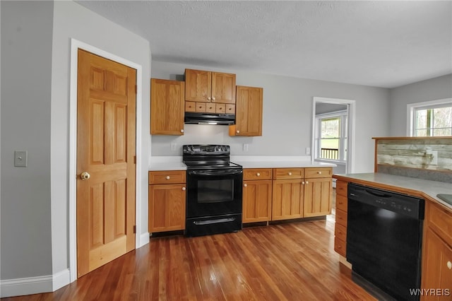 kitchen with exhaust hood, black appliances, light countertops, baseboards, and dark wood-style floors