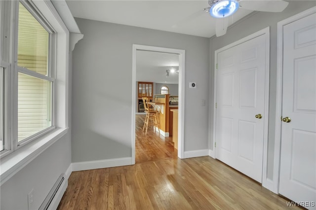 hallway featuring a baseboard radiator, light wood finished floors, and baseboards